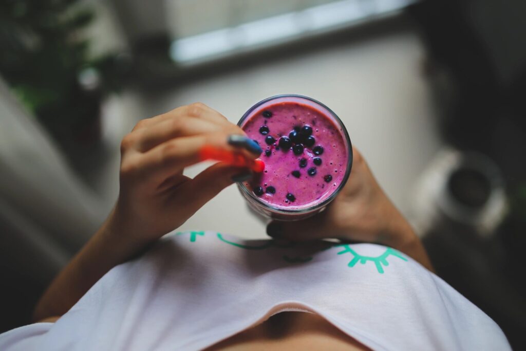 Hands holding a vibrant pink smoothie bowl topped with blueberries.