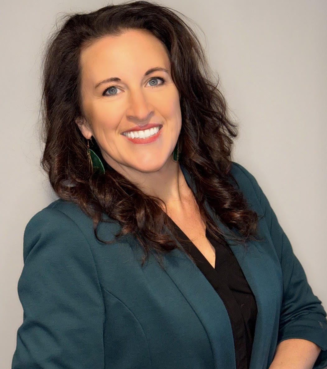 Professional woman smiling confidently in a teal blazer against a plain background.